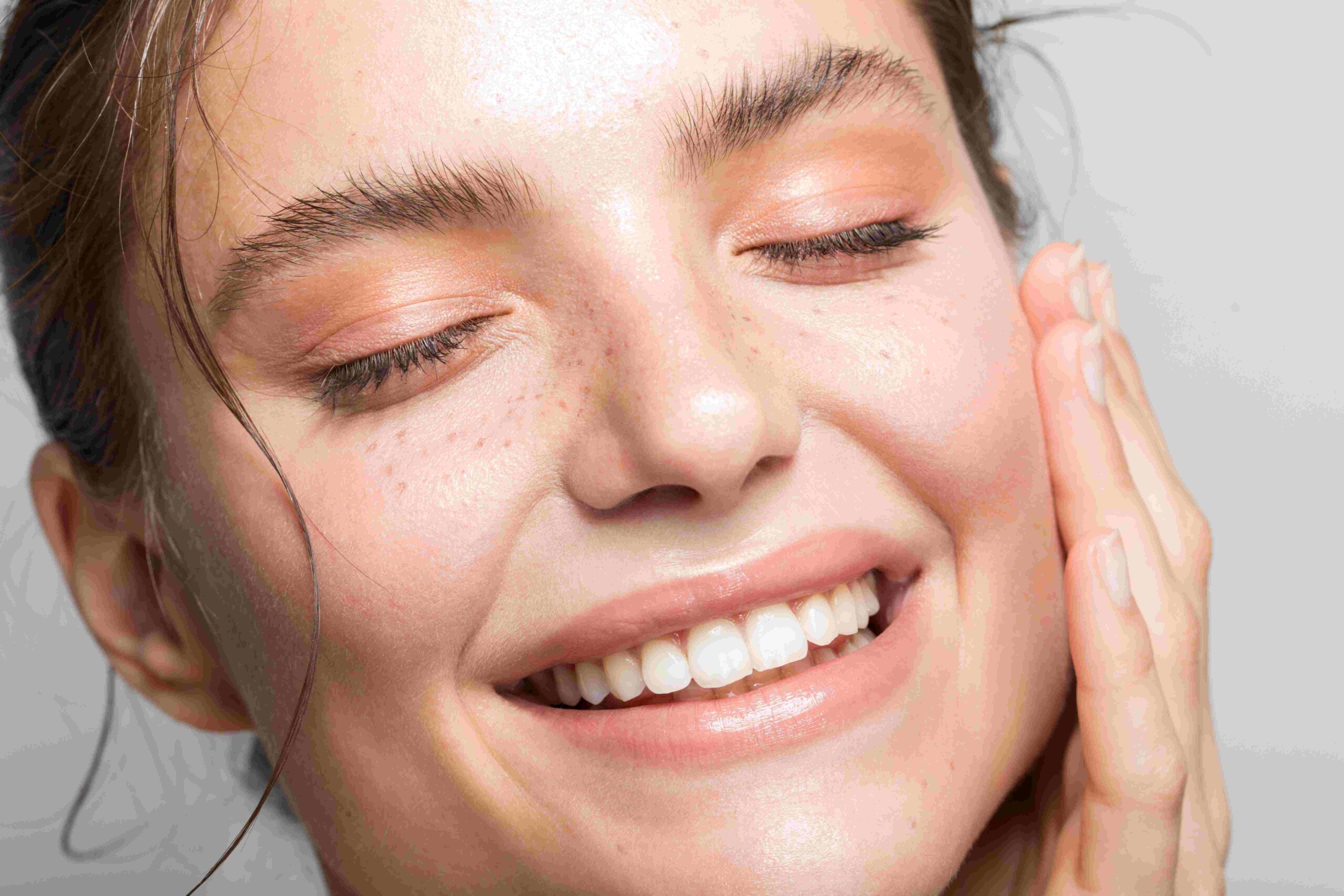 Close up shot of the face of a beautiful woman, one hand on her cheek, with eyes closed and a smile