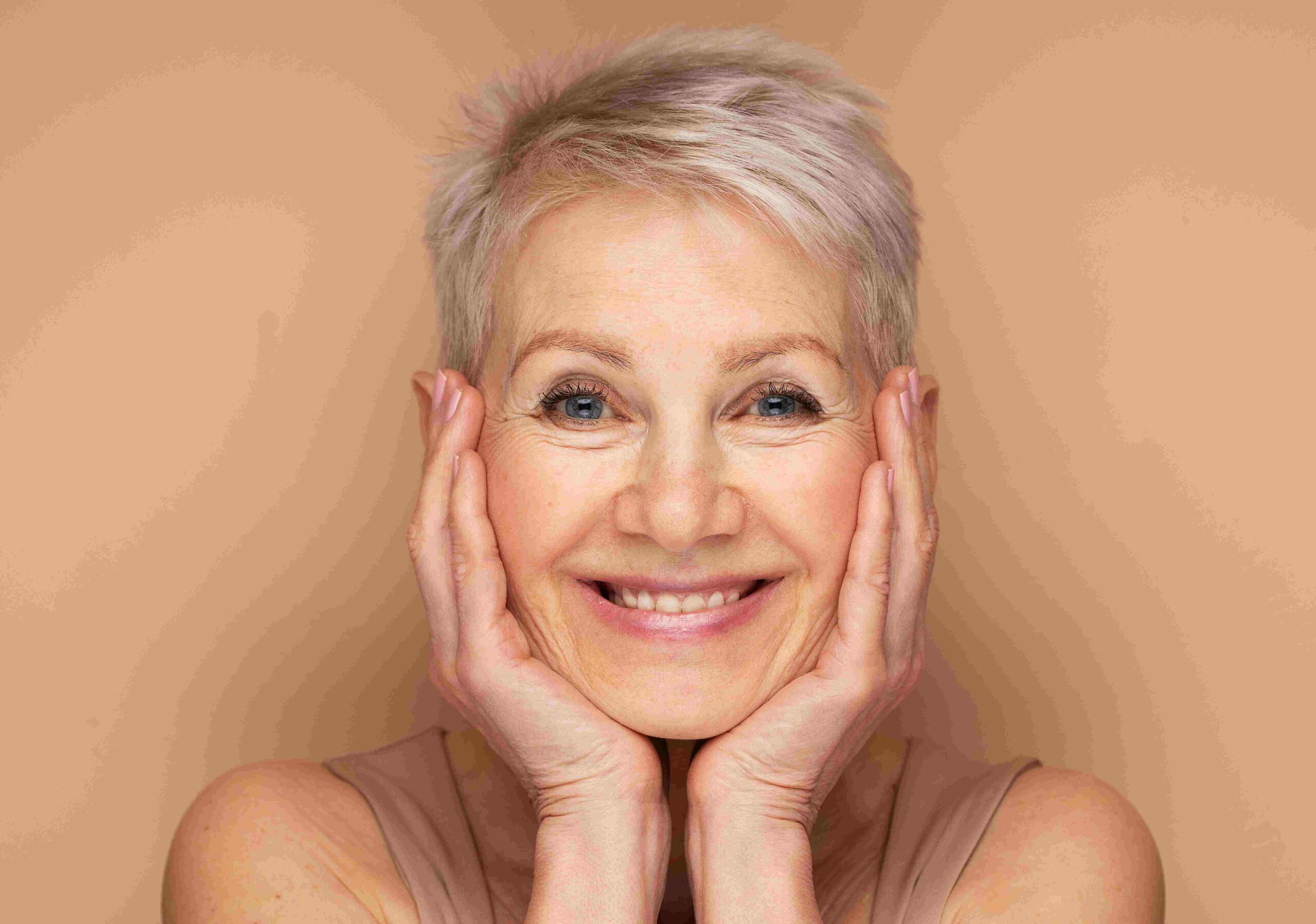 Headshot of a mature woman with silver hand both hands cupping her face with beautiful smile radiating joy