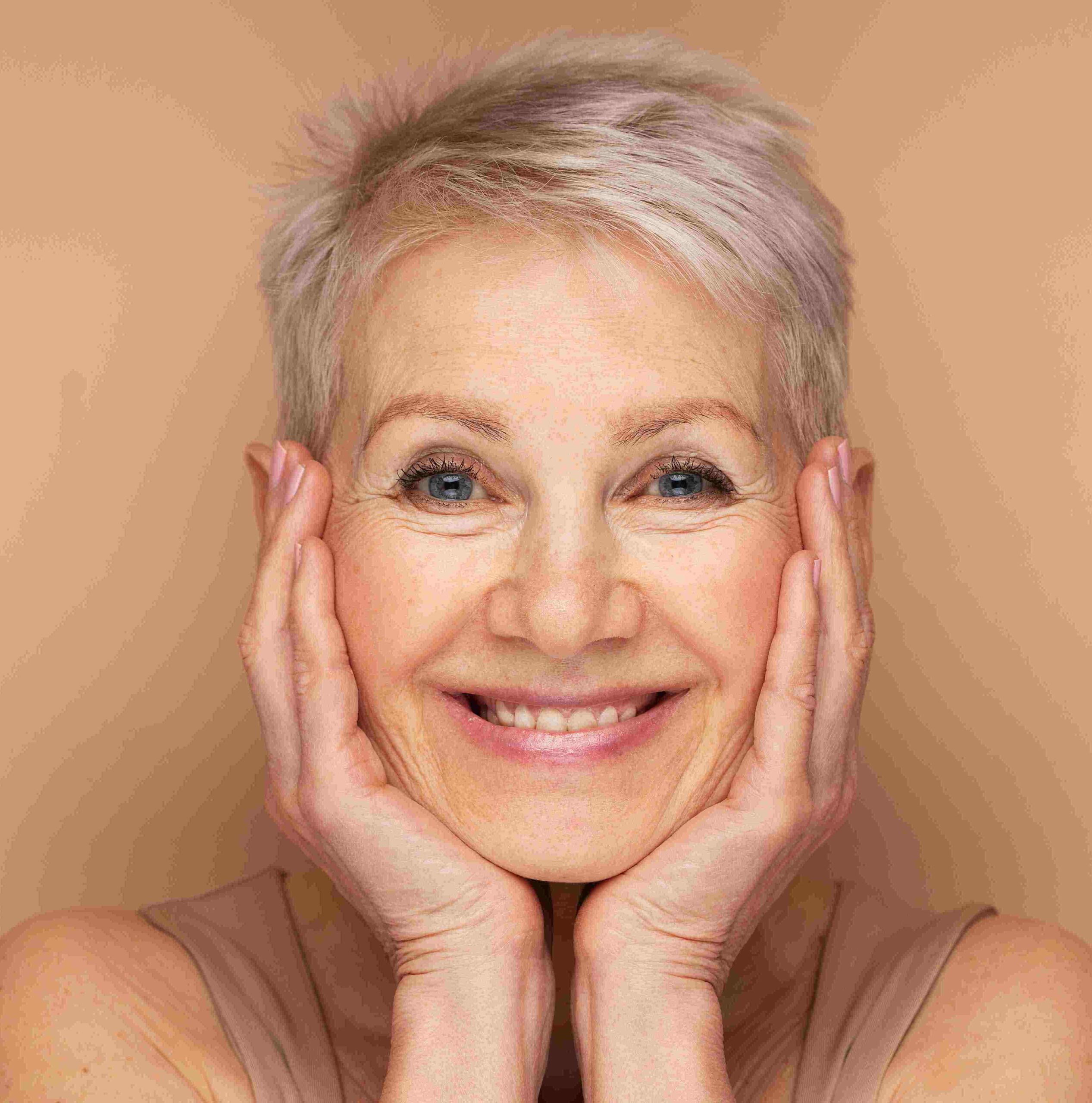 Headshot of a mature woman with silver hand both hands cupping her face with beautiful smile radiating joy