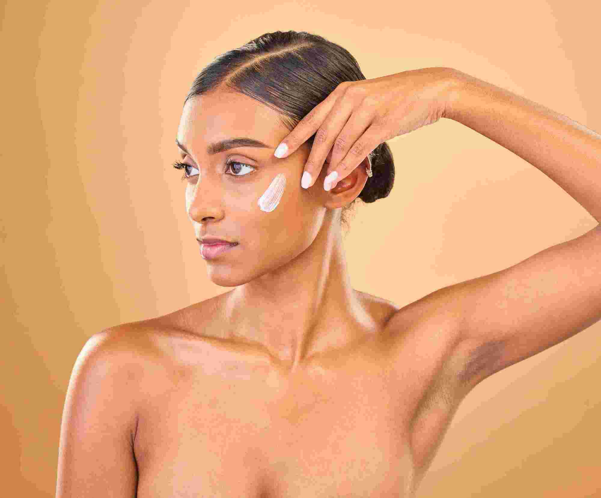 Olive Skin woman showing off nails, putting on white cream on face.