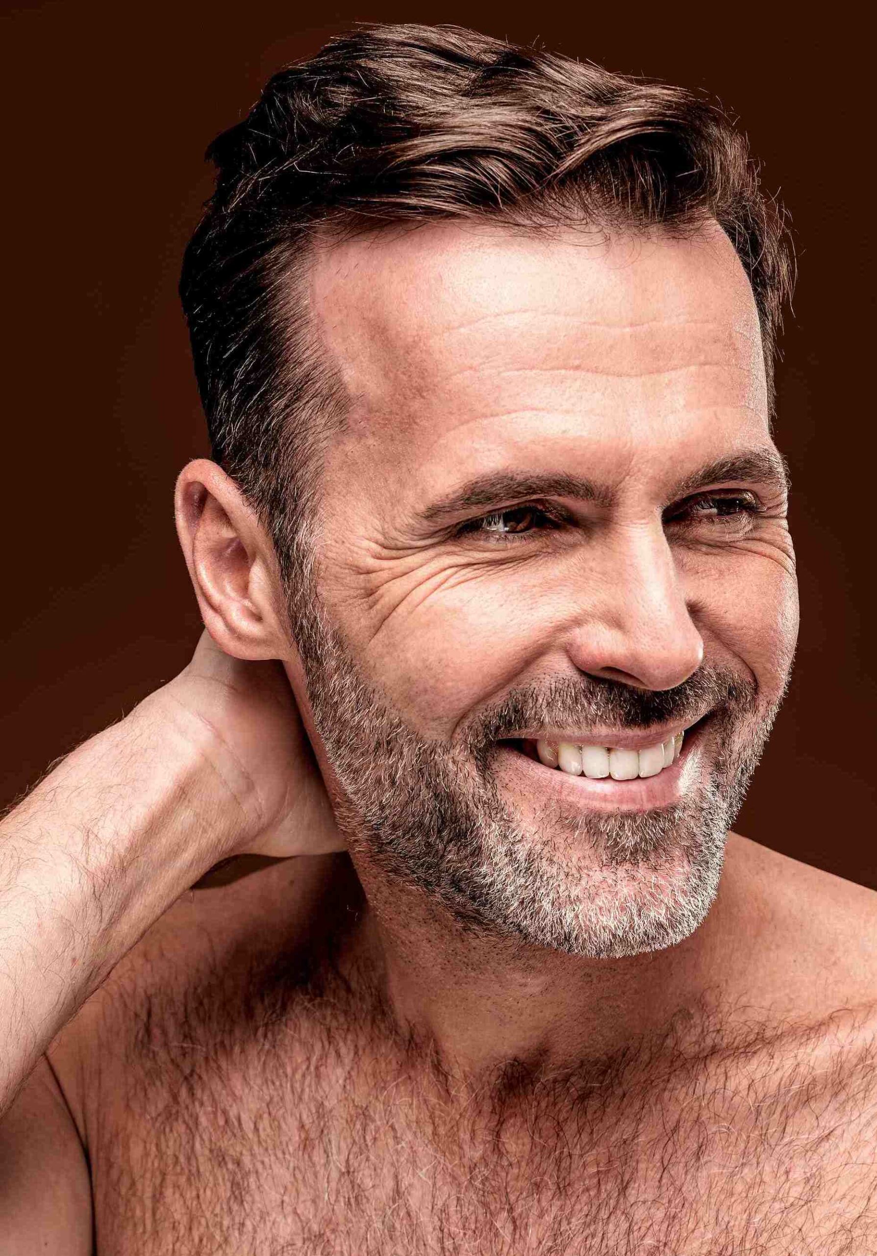 Mature good looking bare shouldered smiling man with hand behind neck