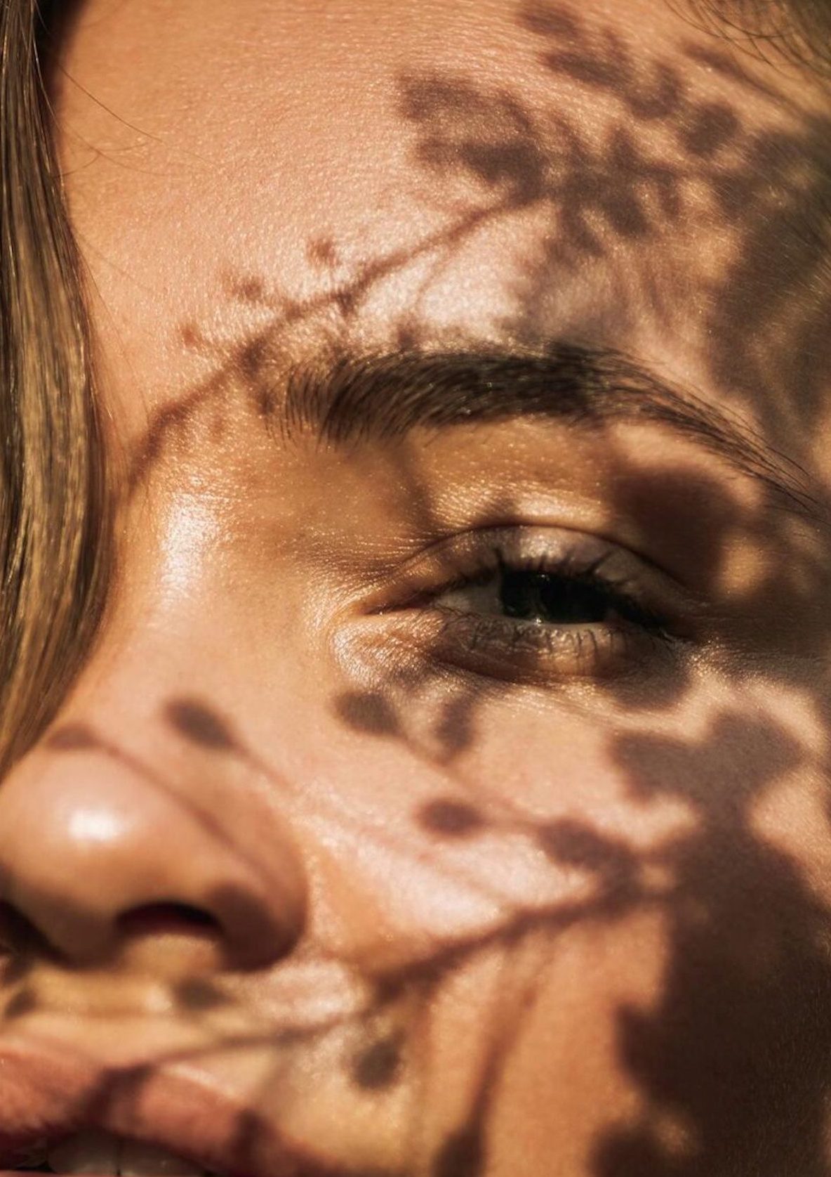 Eursian face with hair covering part of her face and shadows of foliage on rest of the face