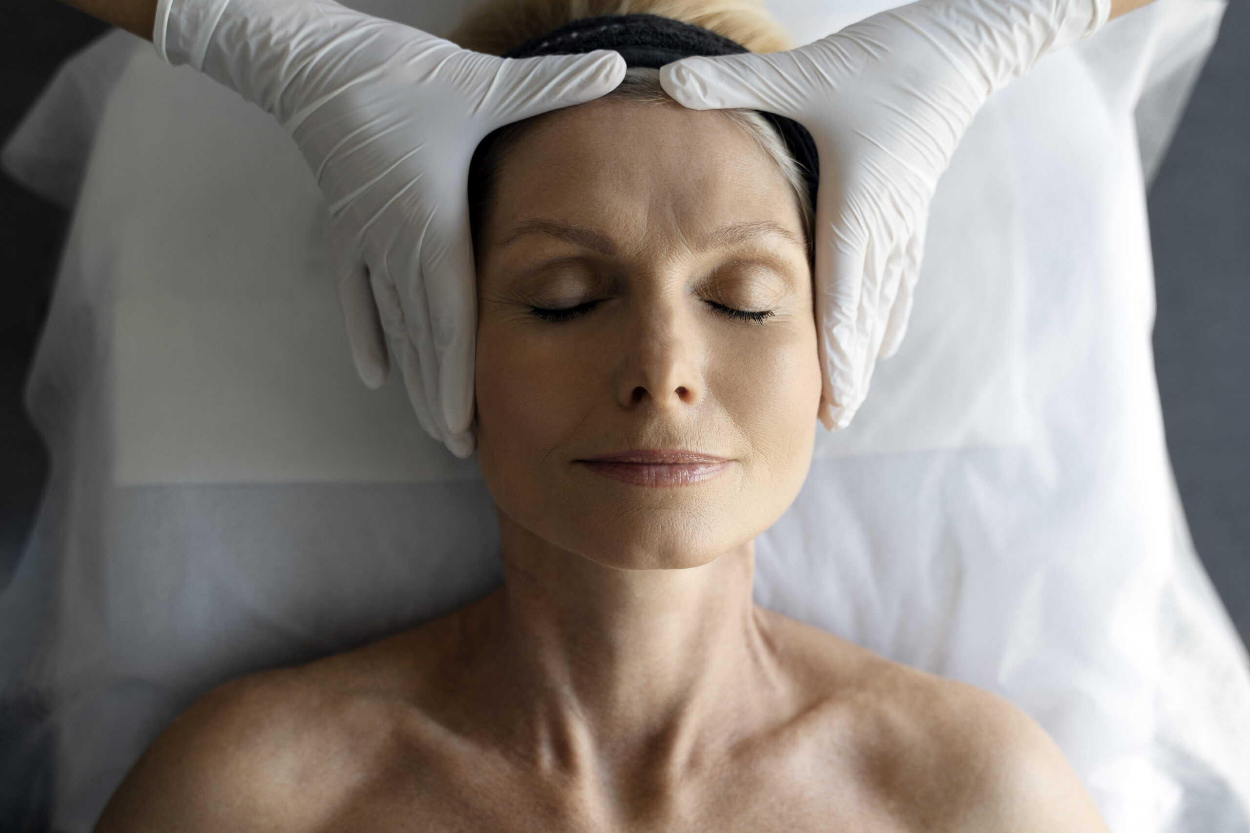 Cosmetologist wearing white protective gloves examining client's face in clinic. She is working with patient and making beauty procedures. Cosmetology concept